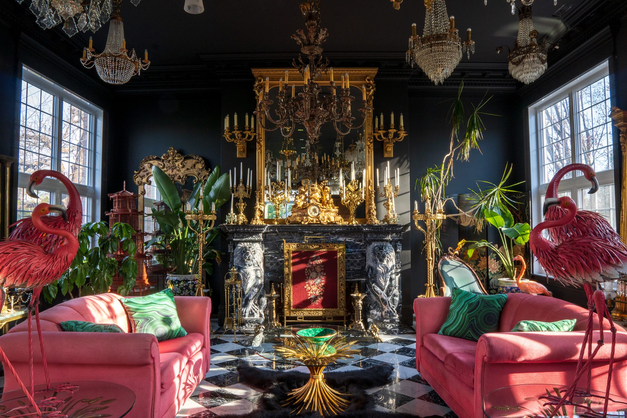 Le grand salon du Manoir Blackswan : murs noirs, lustres de cristal, cheminée de marbre et canapés framboise
