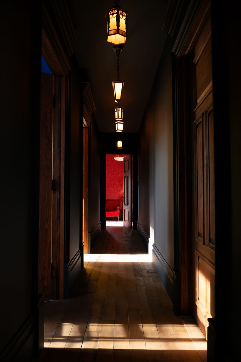 Le corridor du manoir, ses lanternes en enfilade et une chambre rouge au fond