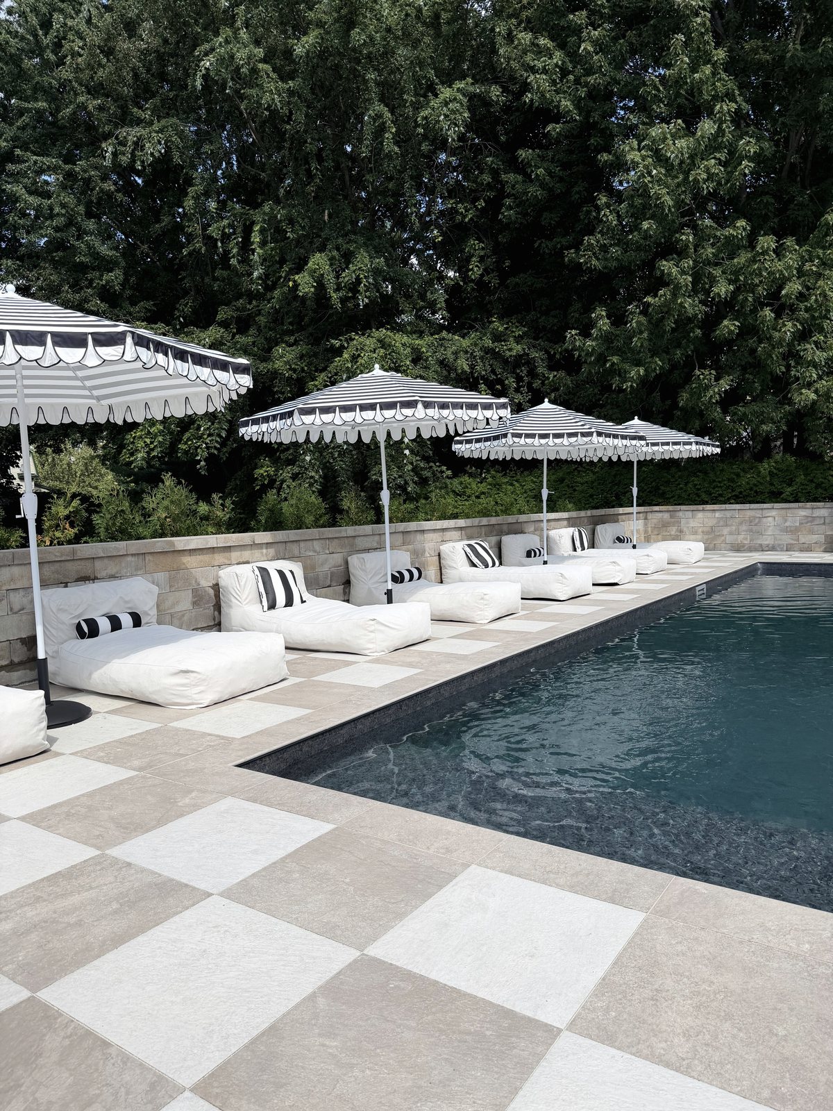 La piscine chauffée du Manoir Blackswan, bordée d'un damier de porcelaine d'Italie, avec ses transats blancs et ses parasols rayés.