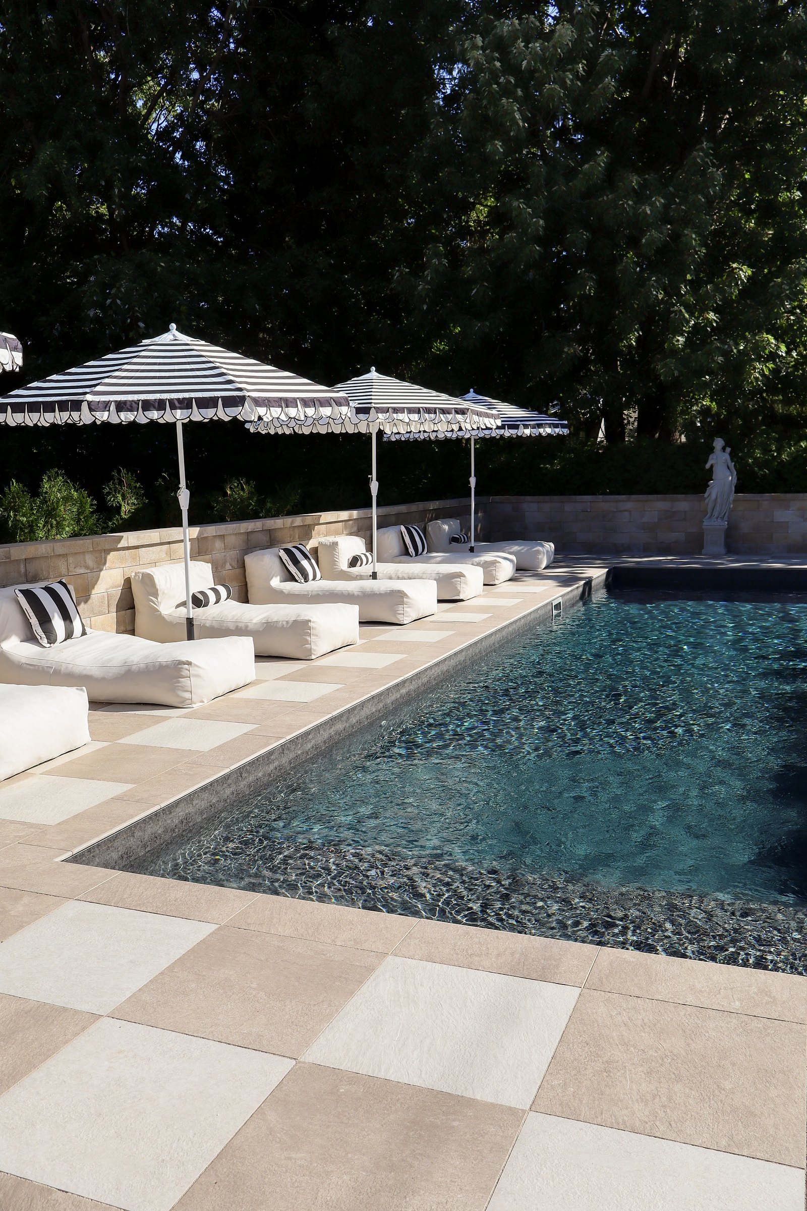 Piscine du domaine, parasols rayés et transats sous les arbres