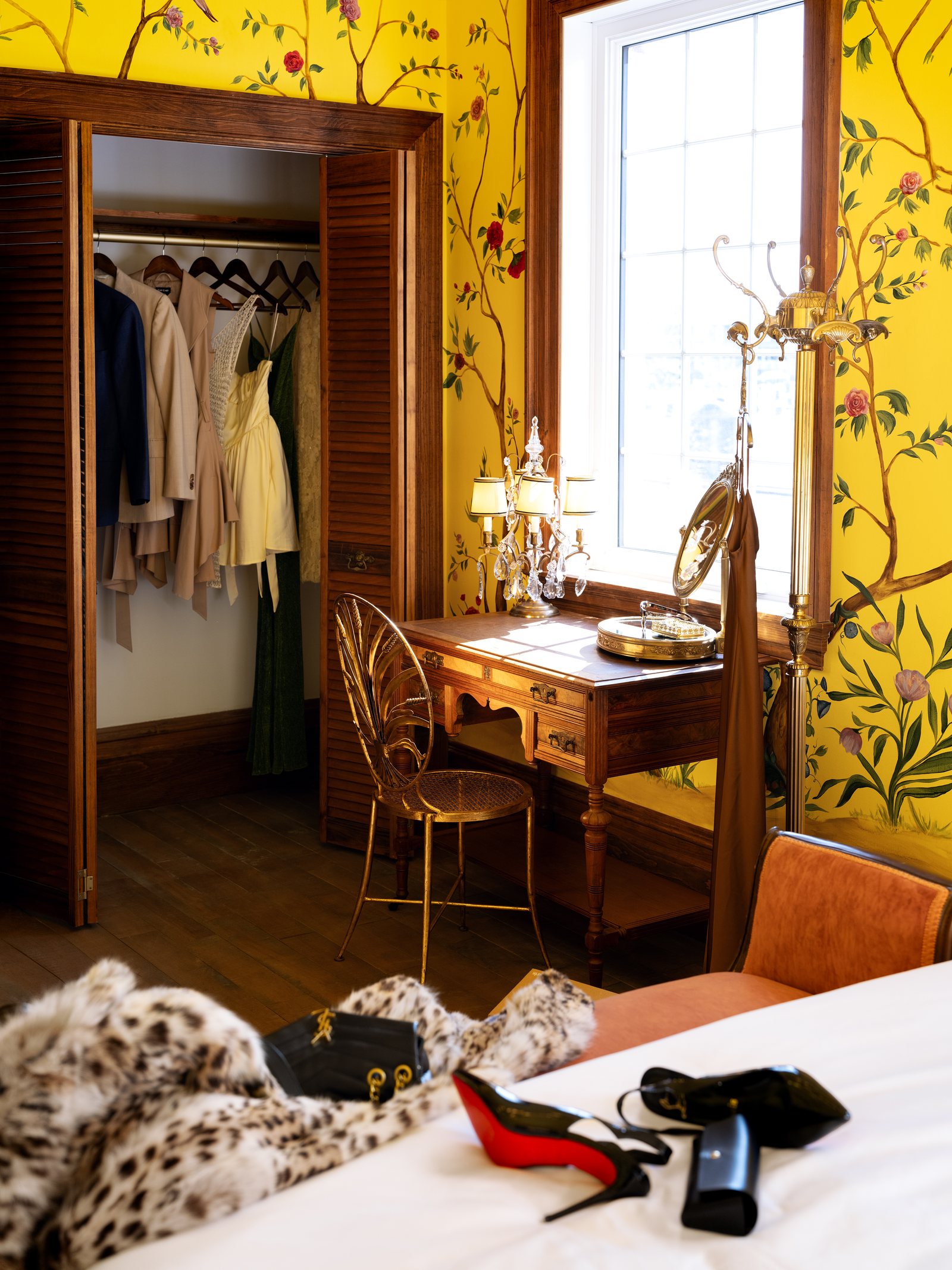 Une chambre du Manoir Blackswan au papier peint jaune à branches fleuries, avec sa coiffeuse et des vêtements suspendus