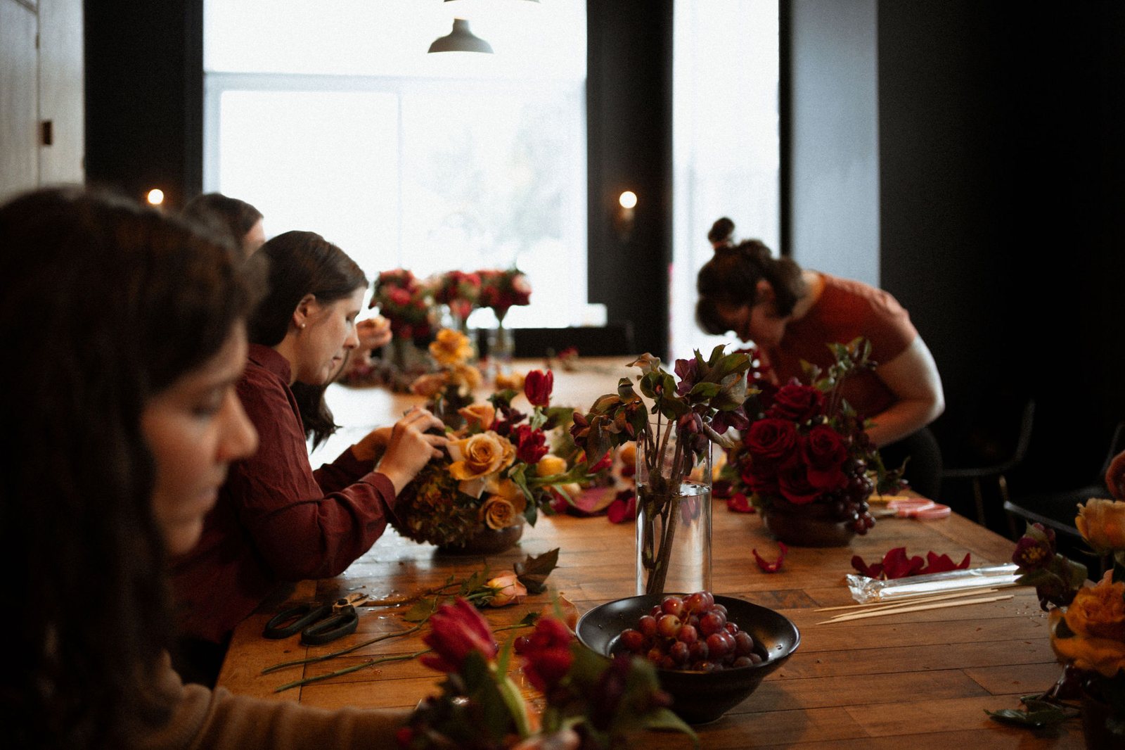 Une fleuriste place des roses dans un arrangement, à la grande table de bois du Manoir Blackswan