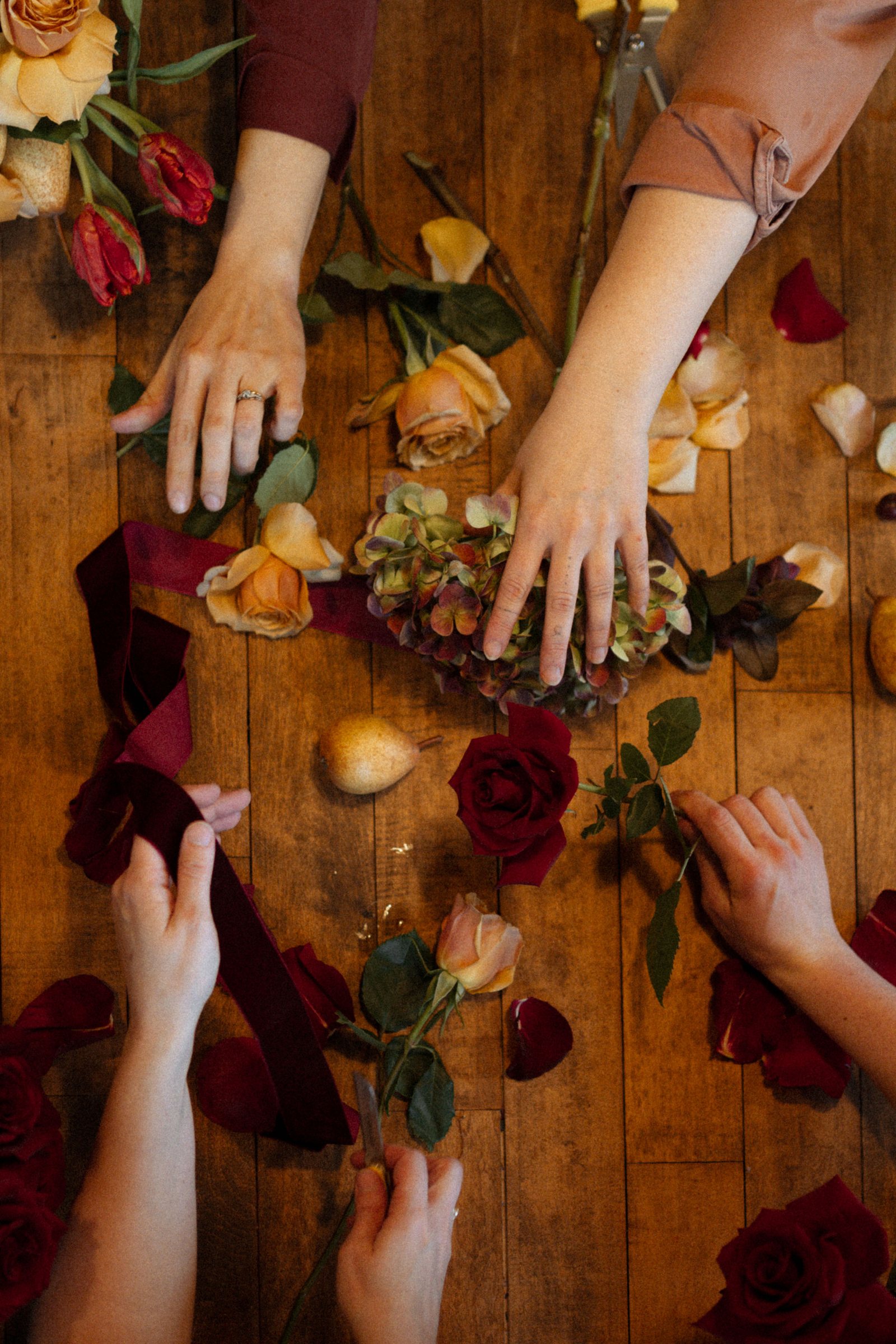 Des mains choisissent des roses, un hortensia et un ruban de velours sur une table de bois, au Manoir Blackswan